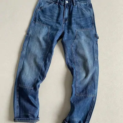 Blue washed carpenter jeans laid flat on a pale floor
