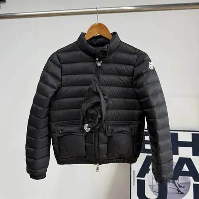A short black puffer jacket on a wooden hanger in front of a grey wall