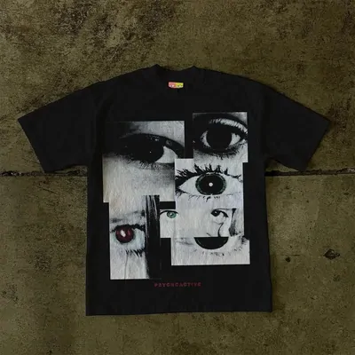 A black T-shirt with a collage print of eyes, laid on a dark floor