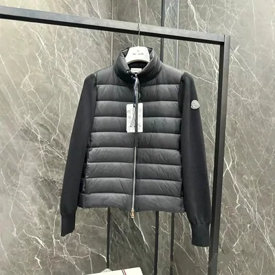 A black quilted jacket with its paper tag still attached, hanging by a mirror